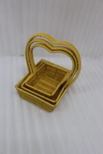 Three yellow handwoven rattan baskets nested together featuring prominent heart-shaped top handles on a wooden table.