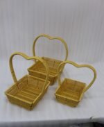 Three yellow handwoven rattan baskets nested together featuring prominent heart-shaped top handles on a wooden table.