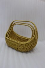 Three yellow handwoven rattan baskets with arch handles nested in a row on a wooden table
