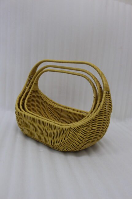 Three yellow handwoven rattan baskets with arch handles nested in a row on a wooden table