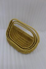 Three yellow handwoven rattan baskets with arch handles nested in a row on a wooden table