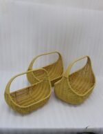 Three yellow handwoven rattan baskets with arch handles nested in a row on a wooden table