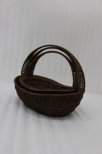 Set of three handwoven dark brown oval rattan baskets with handles resting on a light wooden table.
