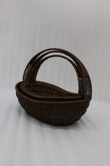 Set of three handwoven dark brown oval rattan baskets with handles resting on a light wooden table.