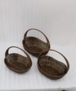Set of three handwoven dark brown oval rattan baskets with handles resting on a light wooden table.