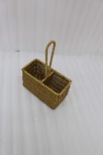 Handwoven rattan spoon holder basket with center handle and two compartments on a wooden table.
