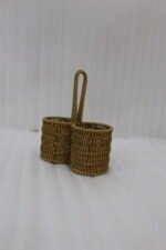 Handmade woven rattan spoon holder with two round caddy compartments and a high center handle on a wooden dining table.