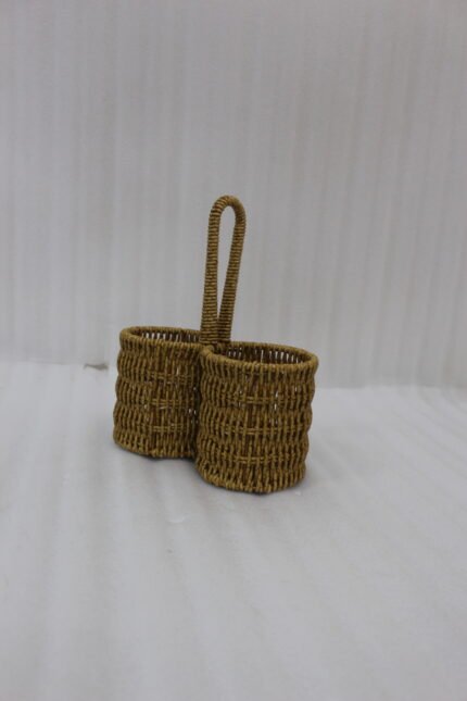 Handmade woven rattan spoon holder with two round caddy compartments and a high center handle on a wooden dining table.