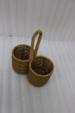 Handmade woven rattan spoon holder with two round caddy compartments and a high center handle on a wooden dining table.
