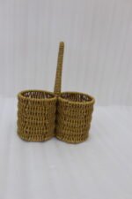 Handmade woven rattan spoon holder with two round caddy compartments and a high center handle on a wooden dining table.
