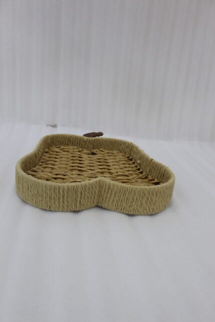 Handwoven light brown rattan fruit dish shaped like an apple resting on a rustic wooden table