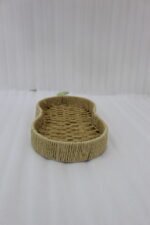 Handwoven pear-shaped rattan fruit dish resting on a light wooden table next to stacked decorative books and a small white vase.