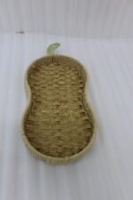 Handwoven pear-shaped rattan fruit dish resting on a light wooden table next to stacked decorative books and a small white vase.