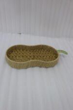Handwoven pear-shaped rattan fruit dish resting on a light wooden table next to stacked decorative books and a small white vase.