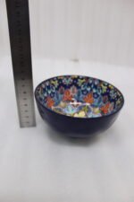 Set of three hand-painted decorative Marrakech ceramic bowls with colorful bohemian patterns and navy blue exteriors on a slate table.