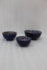 Set of three hand-painted decorative Marrakech ceramic bowls with colorful bohemian patterns and navy blue exteriors on a slate table.