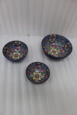 Set of three hand-painted decorative Marrakech ceramic bowls with colorful bohemian patterns and navy blue exteriors on a slate table.