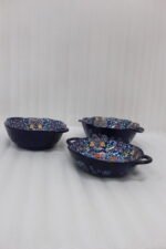 Three hand-painted decorative Marrakech ceramic bowls with intricate bohemian patterns and handles arranged on a dining table runner.