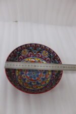 A set of three decorative ceramic bowls in a kitchen. They have rich red exterior glazes and detailed, traditional hand-painted Moroccan-style patterns in blue, yellow, and red on the inside, sitting on a wooden counter next to spice jars.