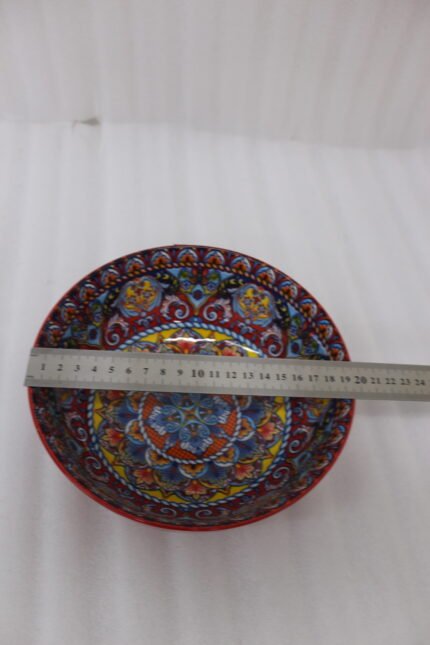 A set of three decorative ceramic bowls in a kitchen. They have rich red exterior glazes and detailed, traditional hand-painted Moroccan-style patterns in blue, yellow, and red on the inside, sitting on a wooden counter next to spice jars.