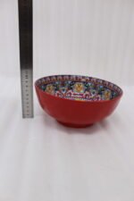 A set of three decorative ceramic bowls in a kitchen. They have rich red exterior glazes and detailed, traditional hand-painted Moroccan-style patterns in blue, yellow, and red on the inside, sitting on a wooden counter next to spice jars.
