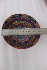 A set of three decorative ceramic bowls in a kitchen. They have rich red exterior glazes and detailed, traditional hand-painted Moroccan-style patterns in blue, yellow, and red on the inside, sitting on a wooden counter next to spice jars.