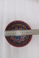 A set of three decorative ceramic bowls in a kitchen. They have rich red exterior glazes and detailed, traditional hand-painted Moroccan-style patterns in blue, yellow, and red on the inside, sitting on a wooden counter next to spice jars.