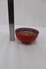 A set of three decorative ceramic bowls in a kitchen. They have rich red exterior glazes and detailed, traditional hand-painted Moroccan-style patterns in blue, yellow, and red on the inside, sitting on a wooden counter next to spice jars.