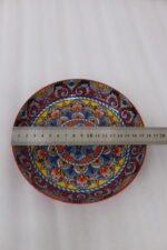 Three vibrant ceramic decorative Moroccan plates featuring intricate mandala patterns in red, blue, and yellow arranged on a wooden countertop.