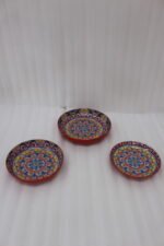 Three vibrant ceramic decorative Moroccan plates featuring intricate mandala patterns in red, blue, and yellow arranged on a wooden countertop.