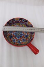 6-inch red ceramic Marrakech serving bowl with vibrant hand-painted geometric interior patterns and a single side handle sitting on a wooden kitchen island