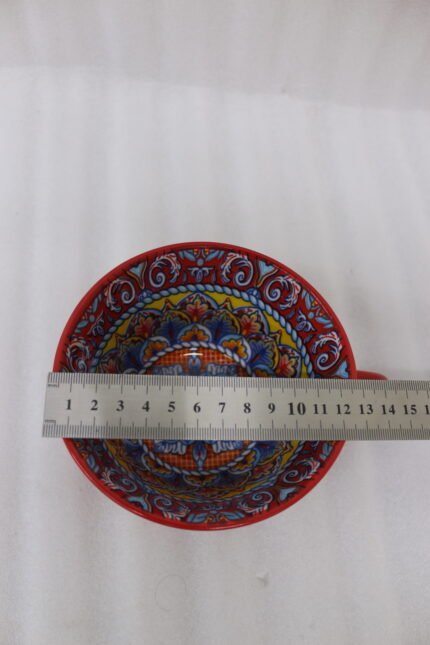 Large red ceramic Marrakech mug with vibrant bohemian interior patterns resting on a round wood slice coaster.