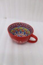 Large red ceramic Marrakech mug with vibrant bohemian interior patterns resting on a round wood slice coaster.