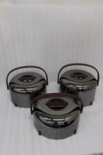 Three modern mirror-finish stainless steel insulated hot pots with wooden arch handles on a kitchen countertop.