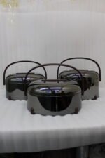 Three modern mirror-finish stainless steel insulated hot pots with wooden arch handles on a kitchen countertop.