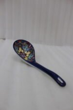 Handcrafted decorative Marrakech ceramic spoon with vibrant blue, yellow, and red bohemian floral patterns resting on a marble countertop