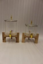 Two ribbed glass beverage dispensers with gold spigots on wooden stands sitting on a kitchen countertop