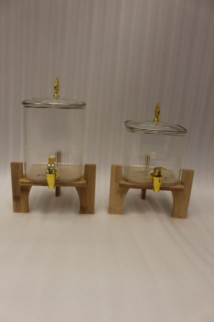Two ribbed glass beverage dispensers with gold spigots on wooden stands sitting on a kitchen countertop