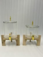 Two ribbed glass beverage dispensers with gold spigots on wooden stands sitting on a kitchen countertop