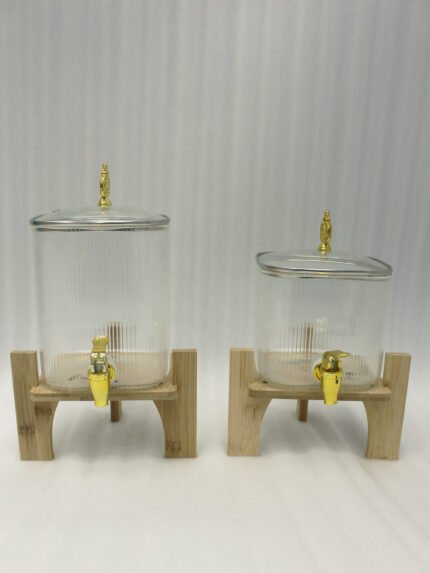 Two ribbed glass beverage dispensers with gold spigots on wooden stands sitting on a kitchen countertop