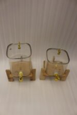 Two ribbed glass beverage dispensers with gold spigots on wooden stands sitting on a kitchen countertop