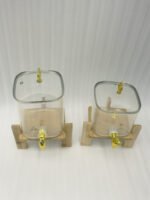 Two ribbed glass beverage dispensers with gold spigots on wooden stands sitting on a kitchen countertop