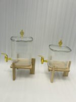 Two ribbed glass beverage dispensers with gold spigots on wooden stands sitting on a kitchen countertop