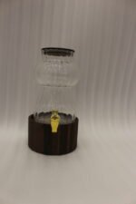 Elegant 3L ribbed glass drink dispenser sitting on a dark wooden base with a gold spigot on a kitchen counter