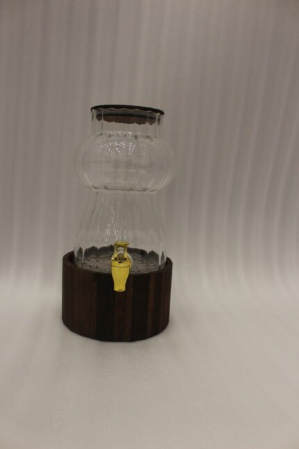 Elegant 3L ribbed glass drink dispenser sitting on a dark wooden base with a gold spigot on a kitchen counter