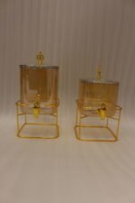 Two amber fluted glass beverage dispensers on gold metal stands resting on a modern kitchen counter