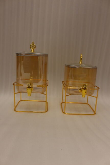 Two amber fluted glass beverage dispensers on gold metal stands resting on a modern kitchen counter