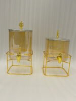 Two amber fluted glass beverage dispensers on gold metal stands resting on a modern kitchen counter