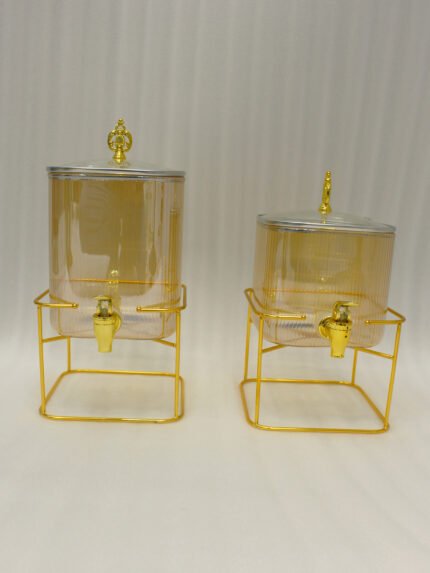 Two amber fluted glass beverage dispensers on gold metal stands resting on a modern kitchen counter