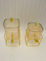 Two amber fluted glass beverage dispensers on gold metal stands resting on a modern kitchen counter